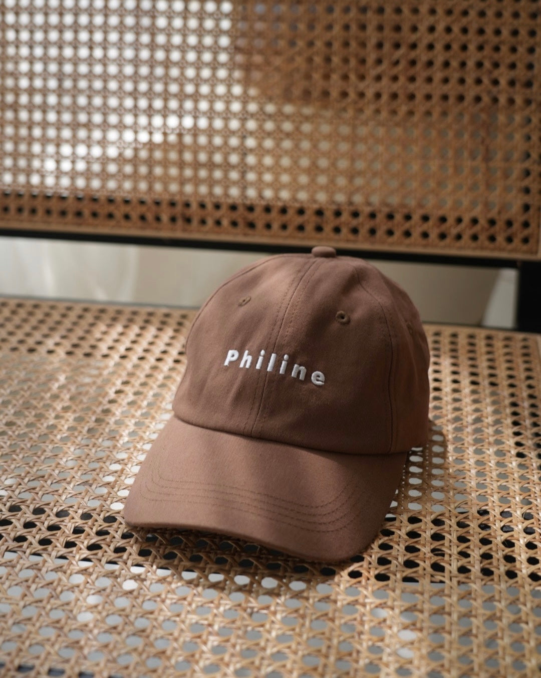 Brown cap with 'Philine' text on a woven surface