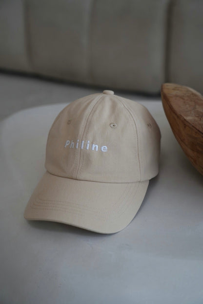 Beige cap with 'Philine' branding on a light surface